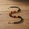 Beaded necklace with black, red, and gold beads on a wooden surface