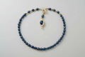 Blue beaded necklace with a gold clasp on a light gray background