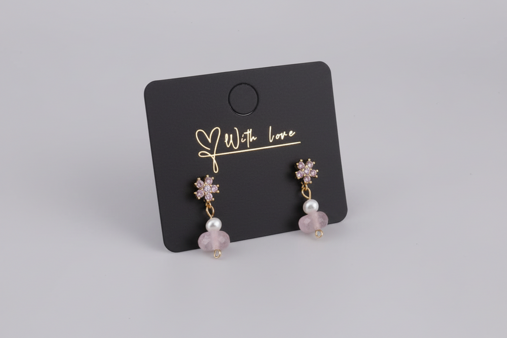 Pair of earrings on a black card with 'With Love' text, displayed on a wooden surface.