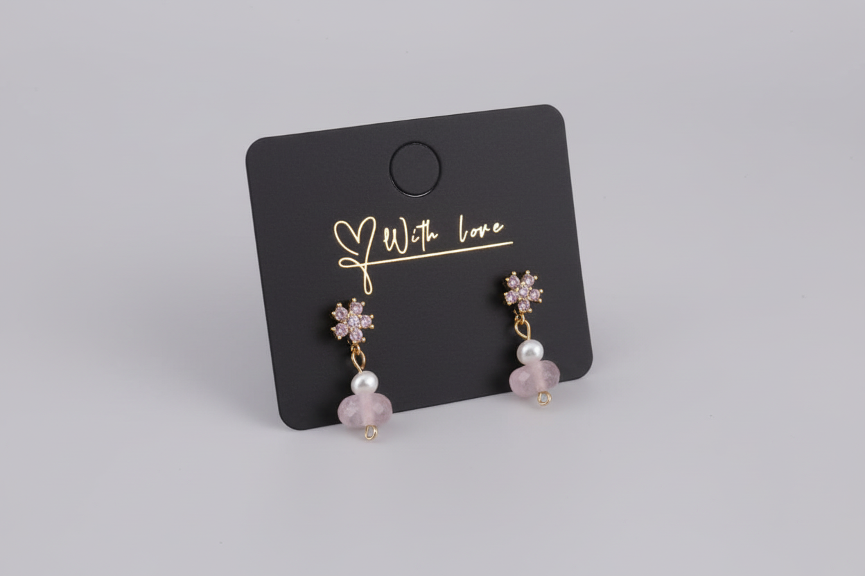 Pair of earrings on a black card with 'With Love' text, displayed on a wooden surface.