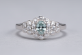 Silver ring with a central blue gemstone and diamond-studded floral design on a light gray background