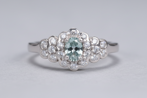 Silver ring with a central blue gemstone and diamond-studded floral design on a light gray background